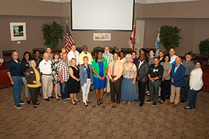 Large group of men and women taking a photo in front of the Orange County Government Chambers Dais